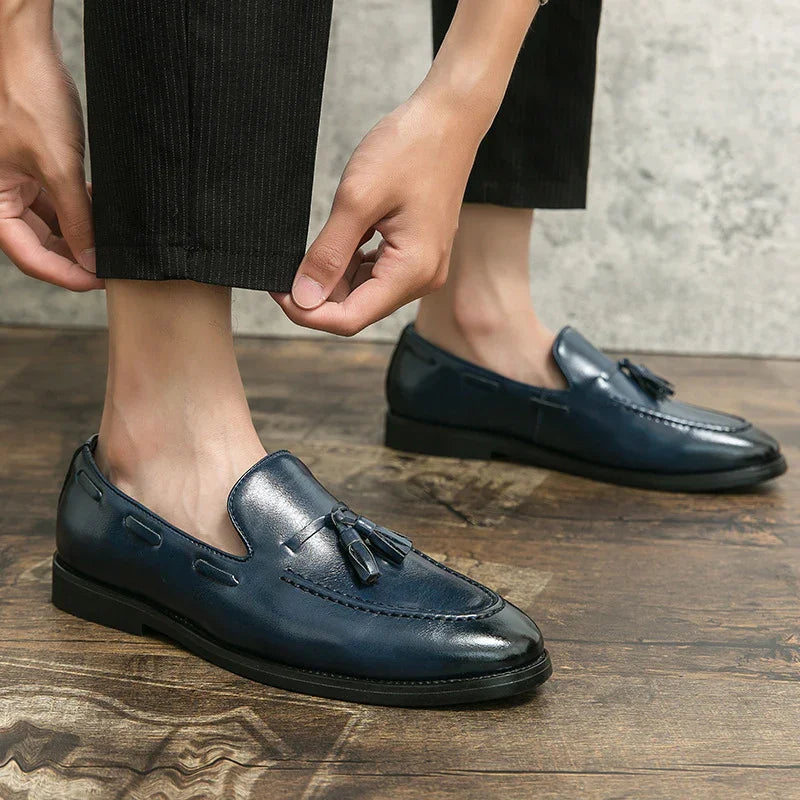 Close-up of person wearing navy blue leather tassel loafers on wooden floor