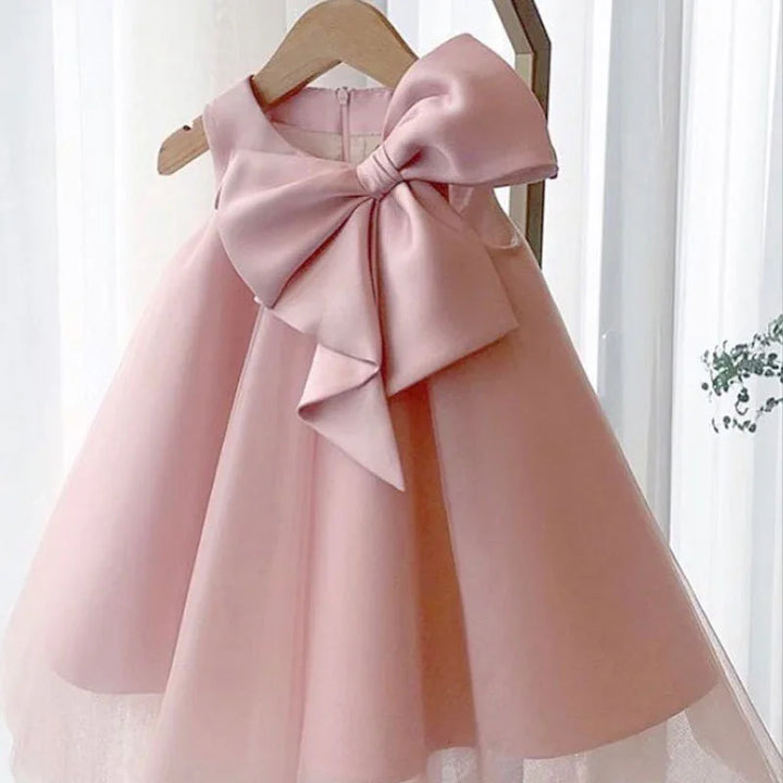 Elegant pink sleeveless baby dress with large bow on wooden hanger in bright room
