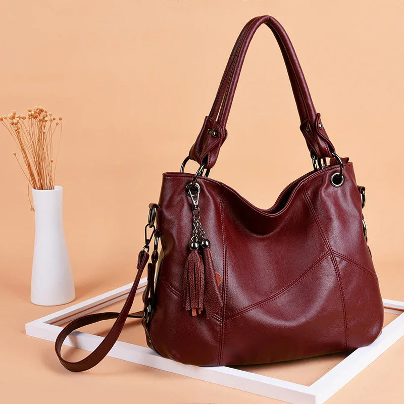 Stylish maroon leather handbag with tassel charm displayed on peach background with white frame and vase