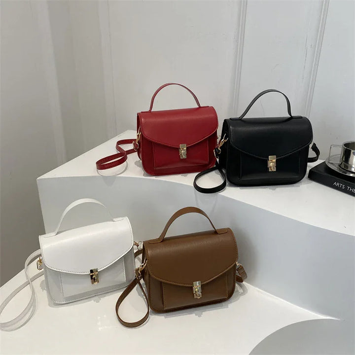 Four small leather handbags in red, black, white, and brown with top handles and gold locks displayed on white geometric stands