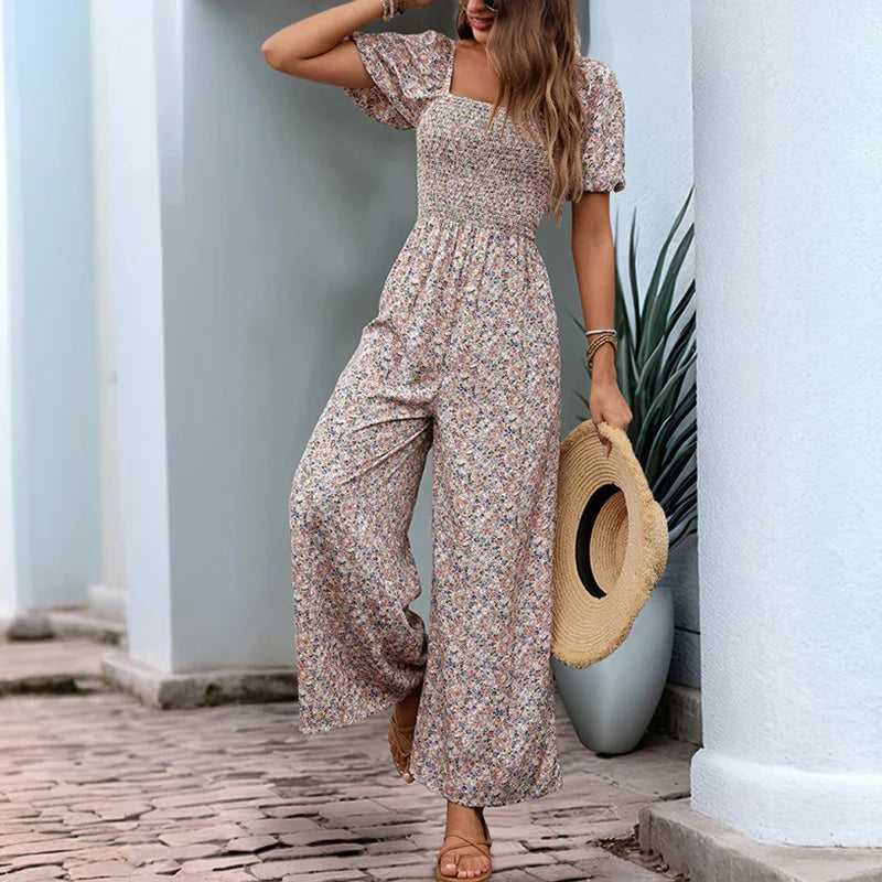 Woman wearing floral wide-leg jumpsuit with puff sleeves holding straw hat outdoors