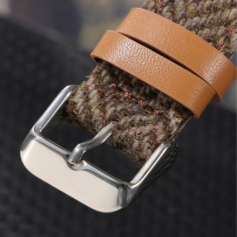 Close-up of a watch strap with textured fabric and tan leather loops secured by a polished metal buckle