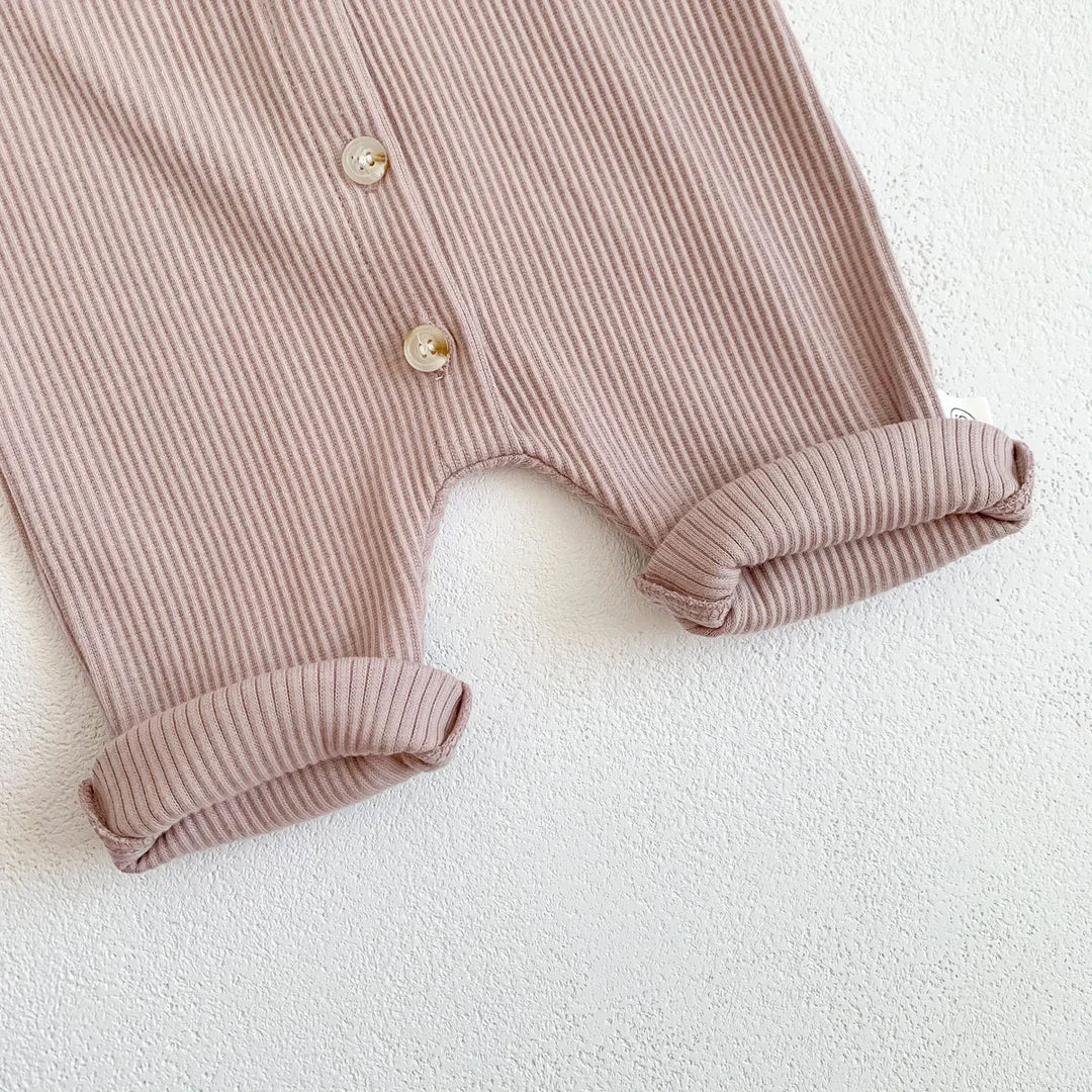 Close-up of folded ribbed pink baby romper with buttons on white textured background