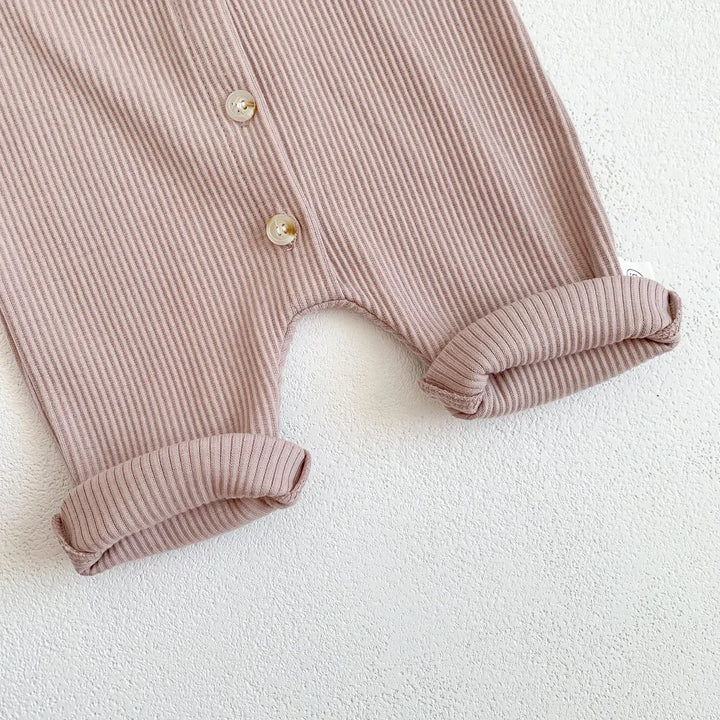 Close-up of folded ribbed pink baby romper with buttons on white textured background