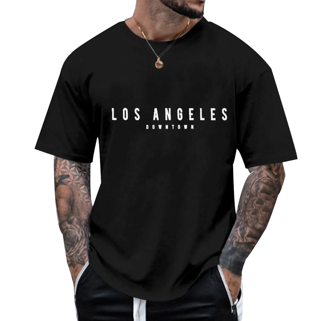 Man wearing black t-shirt with white 'Los Angeles Downtown' text, tattooed arms, and necklace