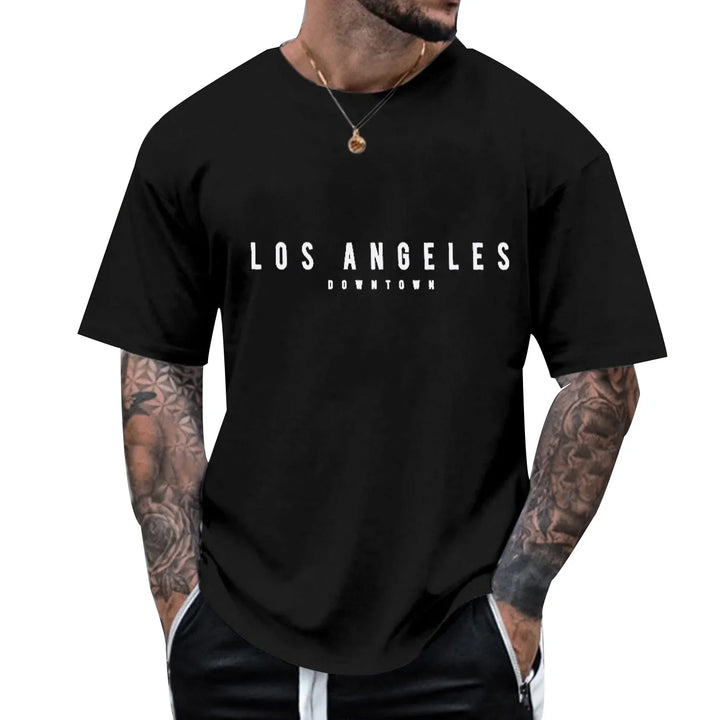 Man wearing black t-shirt with white 'Los Angeles Downtown' text, tattooed arms, and necklace
