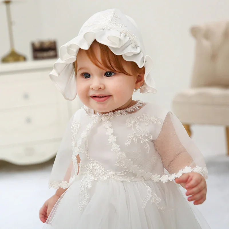 Smiling toddler girl in white embroidered dress and matching bonnet in bright indoor setting