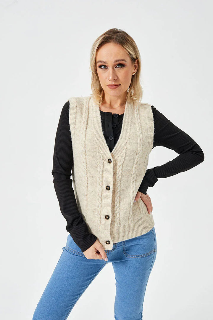 Blonde woman wearing beige cable knit buttoned vest over black long sleeve top and blue jeans on white background