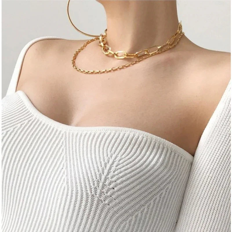Close-up of a woman wearing a white ribbed knit off-shoulder top with layered gold chain necklaces