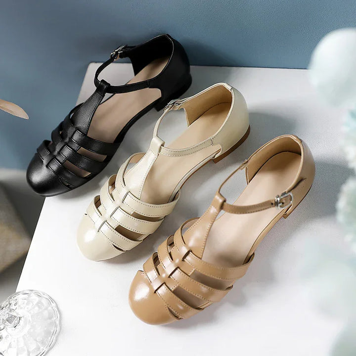 Three women's T-strap leather sandals in black, cream, and tan on a white surface