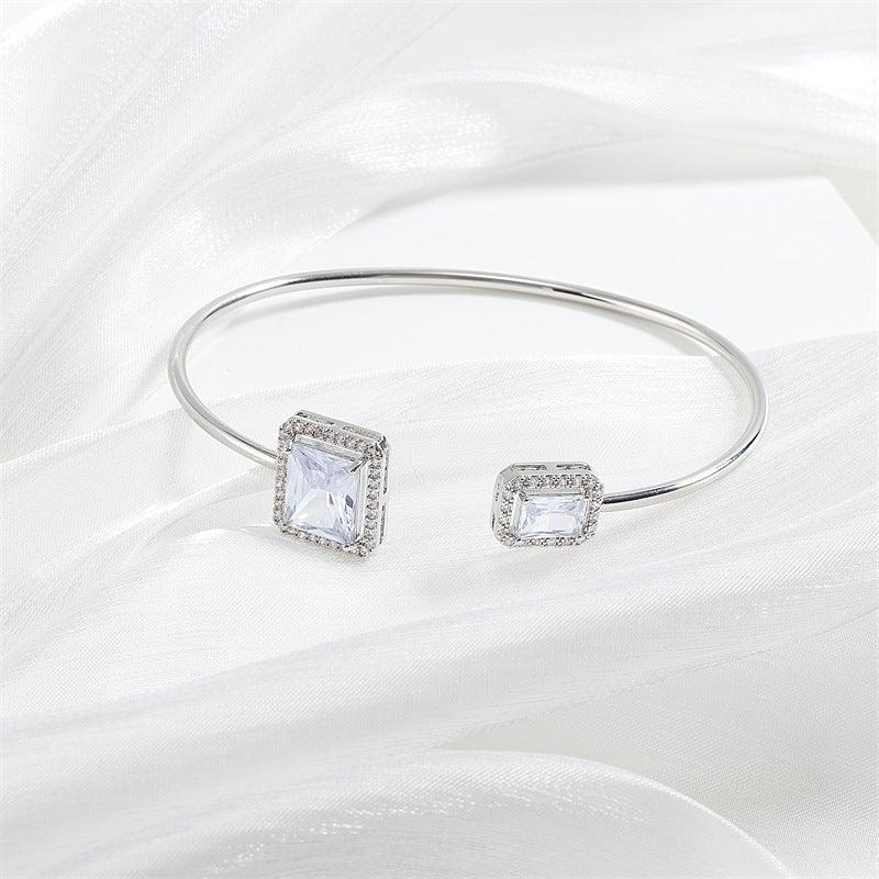 Elegant silver open bangle bracelet with square-cut clear gemstones on white fabric