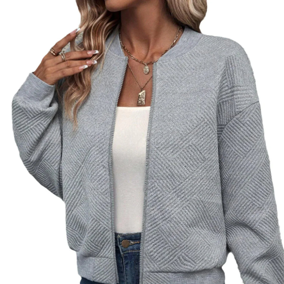 Woman wearing a grey textured knit zip-up cardigan over white top with layered gold necklaces