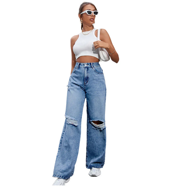 Woman wearing white cropped tank top and high-waisted ripped blue wide-leg jeans with white sneakers