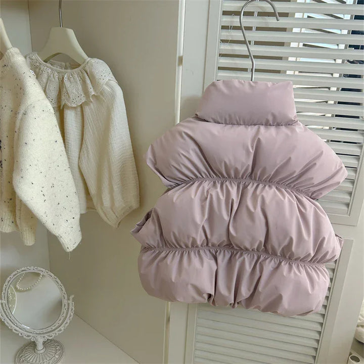 Pink padded sleeveless jacket hanging beside cream knit sweaters on wooden hangers