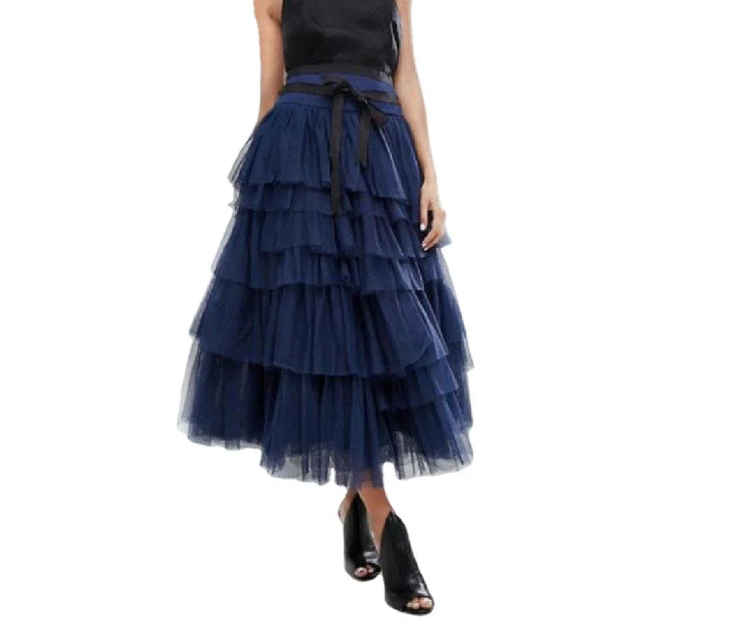 Woman wearing a navy blue tiered tulle midi skirt with black ribbon belt and black open-toe heels