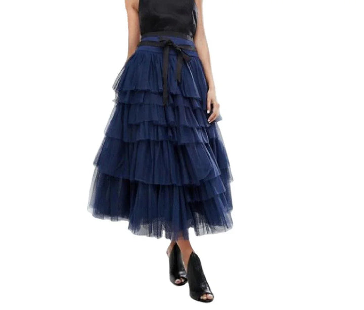 Woman wearing a navy blue tiered tulle midi skirt with black ribbon belt and black open-toe heels