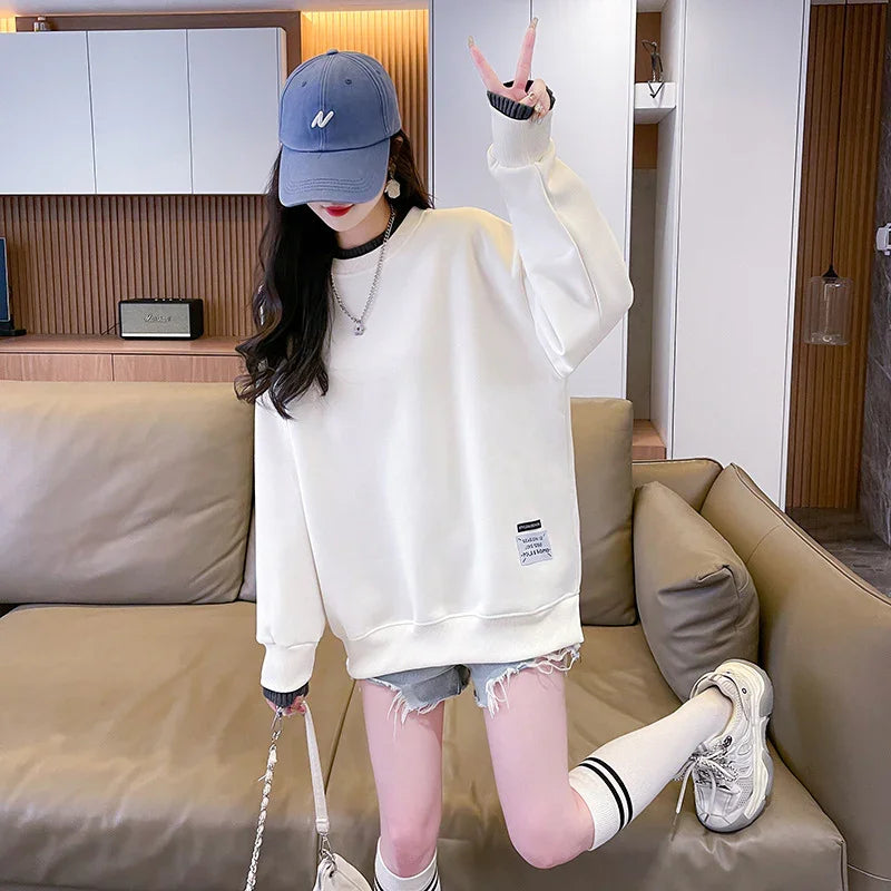 Woman wearing oversized white sweatshirt, distressed denim shorts, blue cap, knee-high socks, and sneakers indoors