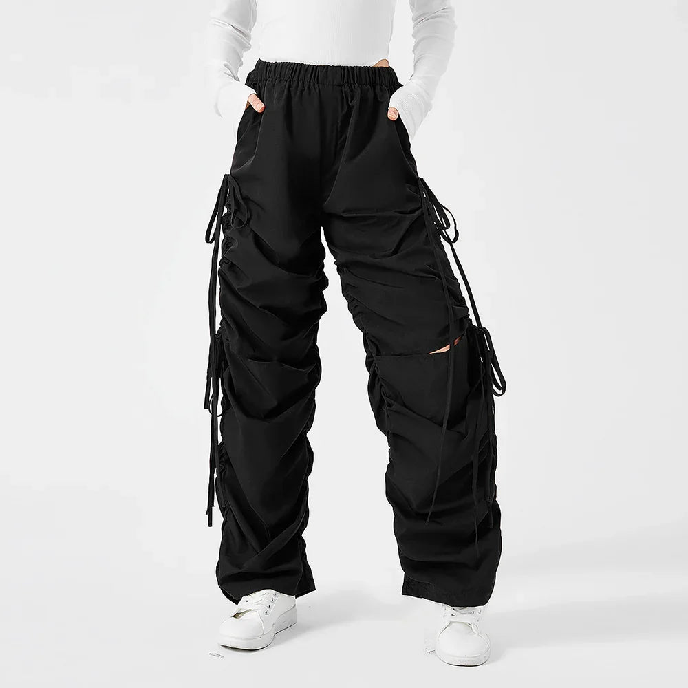 Person wearing black ruched cargo pants with drawstrings and white sneakers on white background