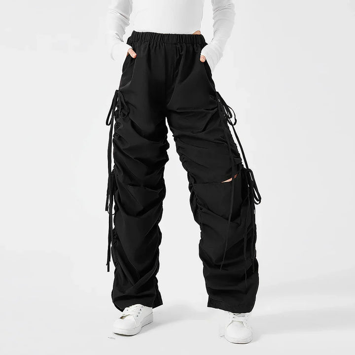 Person wearing black ruched cargo pants with drawstrings and white sneakers on white background