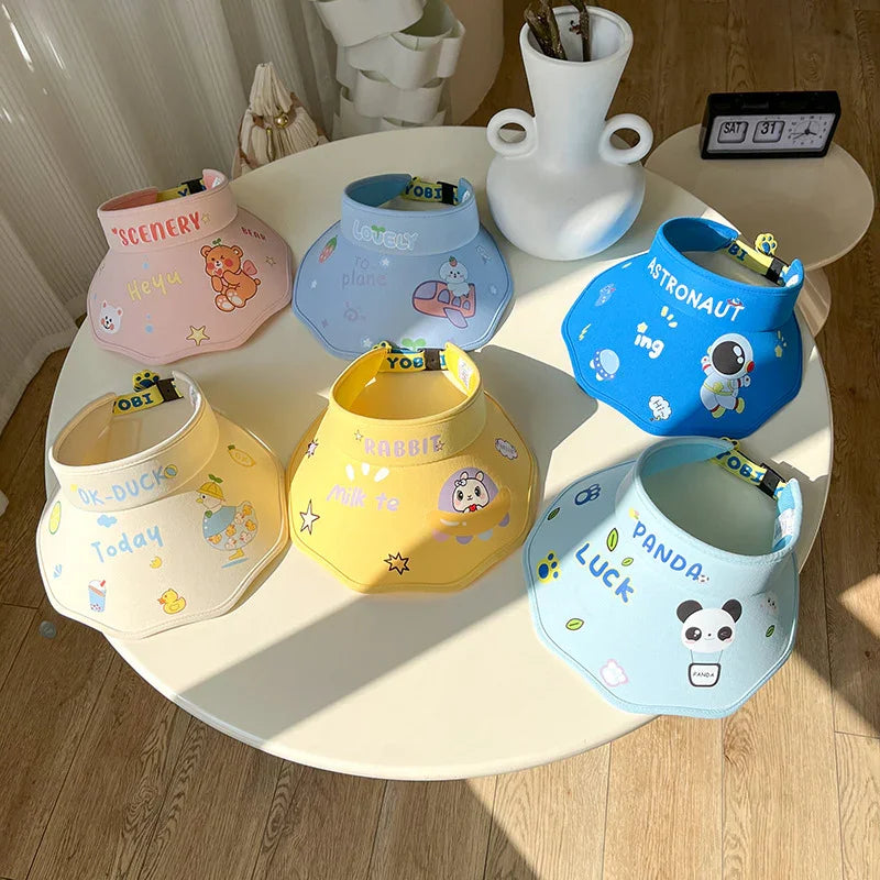 Six colorful animal-themed sun visors on a white round table with wooden floor and decorative vase