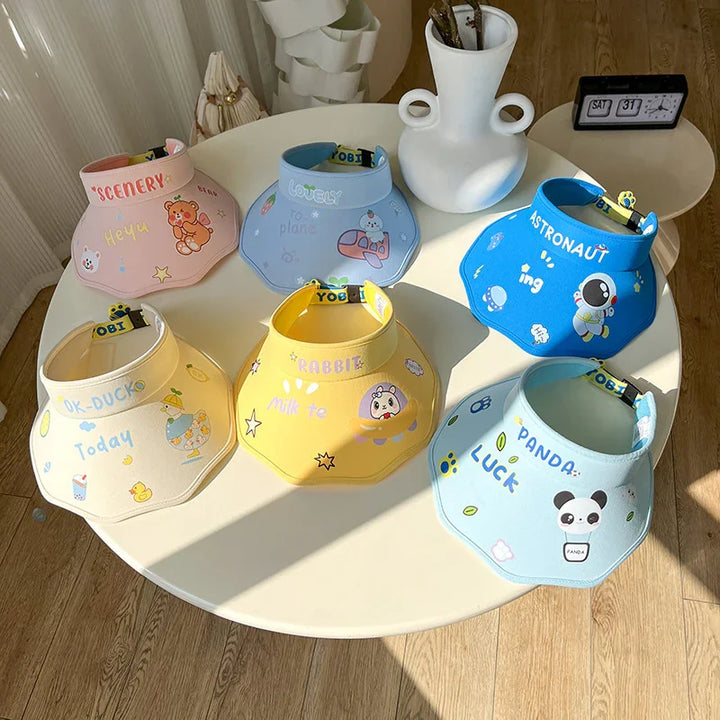Six colorful animal-themed sun visors on a white round table with wooden floor and decorative vase