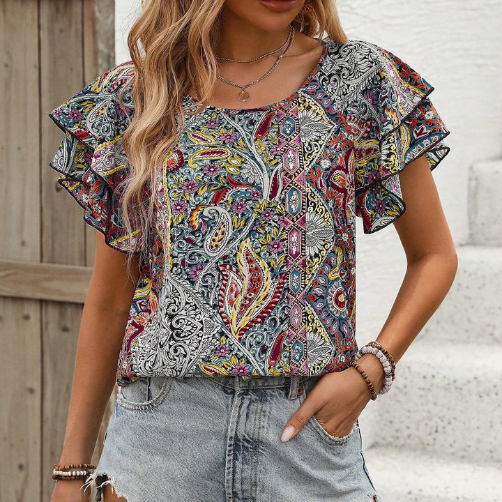 Woman wearing colorful paisley print ruffle sleeve blouse with denim shorts and bracelets