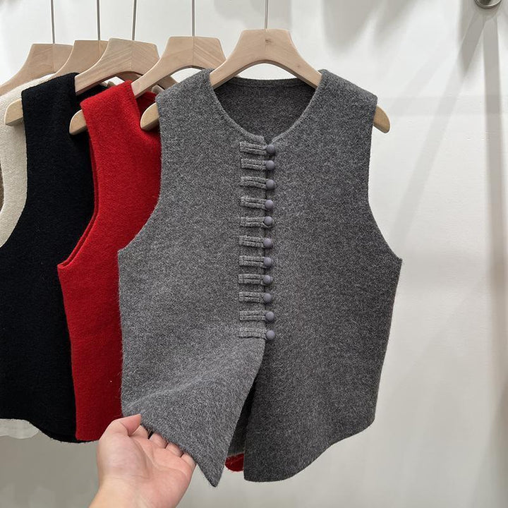 Hand holding soft gray wool sleeveless vest with button details, with red, black, and beige vests hanging on wooden hangers