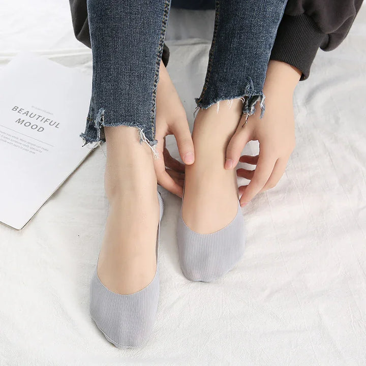 Close-up of feet wearing gray no-show socks with frayed hem blue jeans on white fabric background