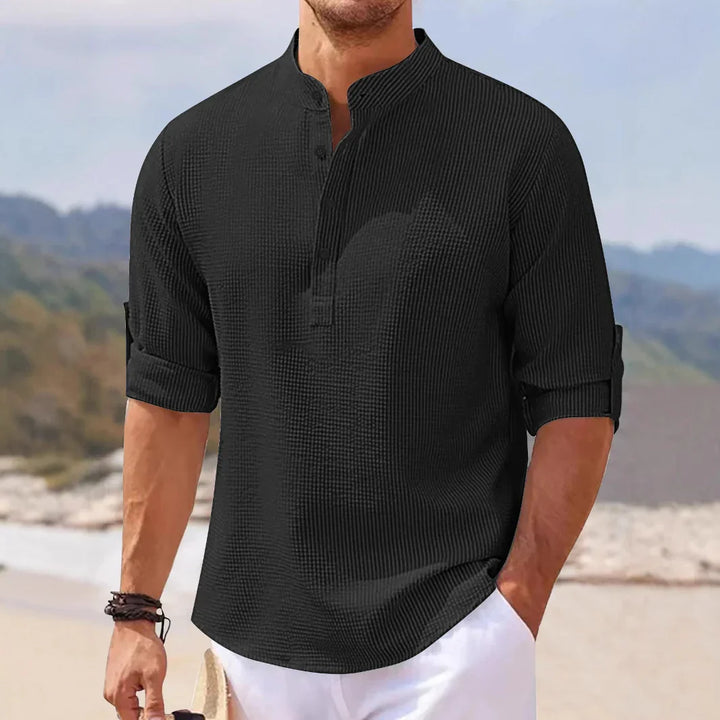 Man wearing black textured casual shirt with rolled-up sleeves and white pants at beach