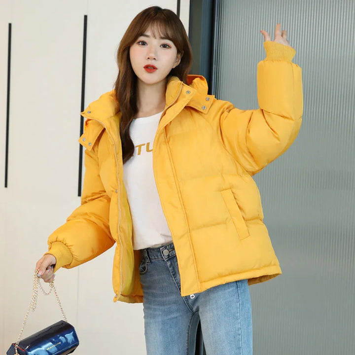 Woman wearing bright yellow puffer jacket with hood, white shirt, blue jeans, holding black handbag