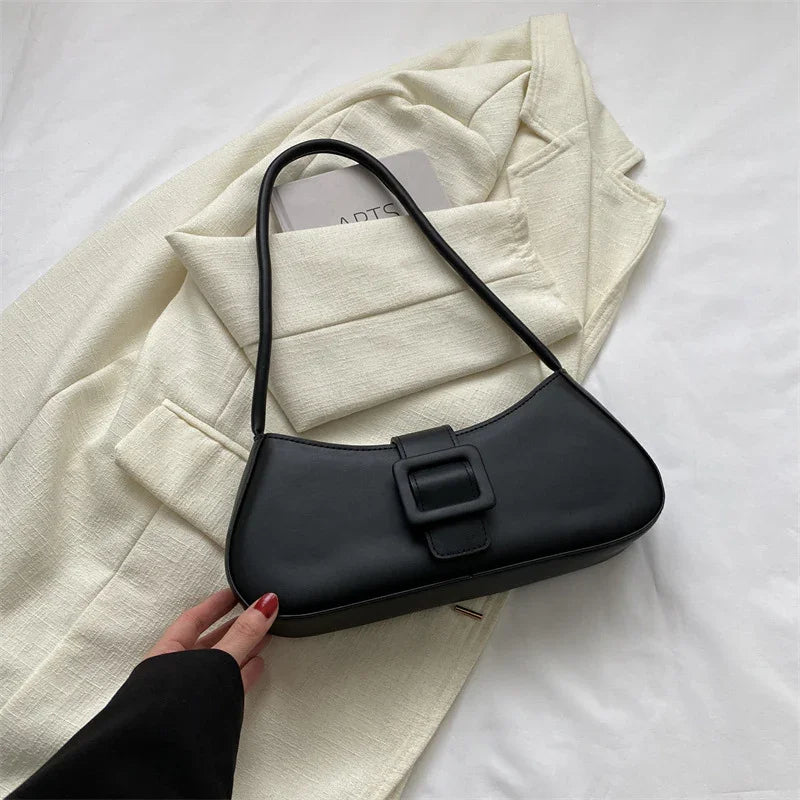 Black leather shoulder bag with buckle detail on cream blazer background