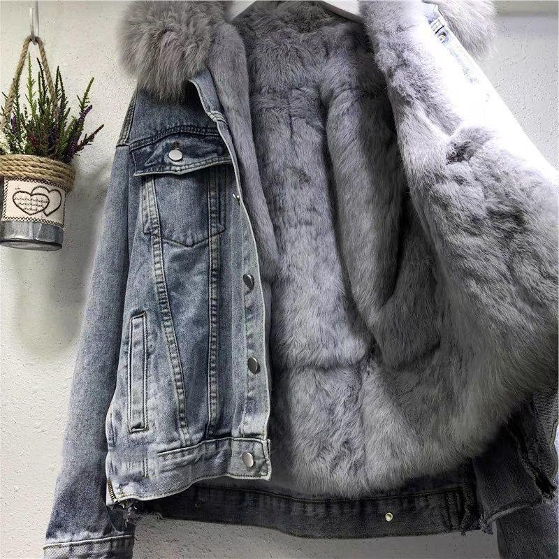 Gray denim jacket with plush gray fur lining and fur collar hanging on wall next to a small potted plant