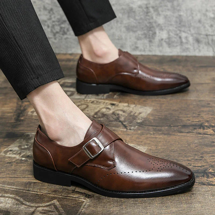 Men's brown leather monk strap dress shoes on wooden floor with black trousers