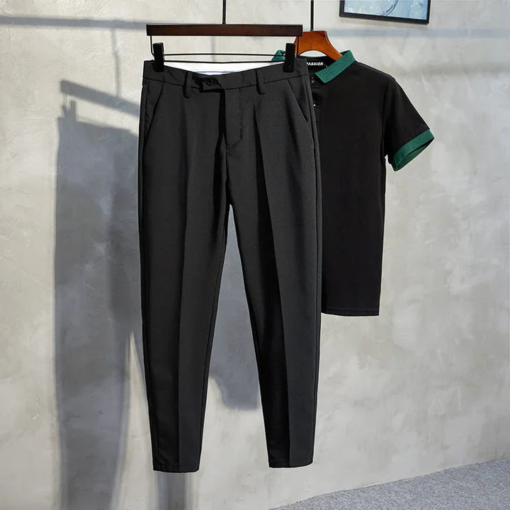 Black tailored pants with front pleats hanging next to black polo shirt with green collar and sleeve cuffs