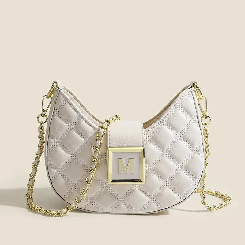 Cream quilted crescent shoulder bag with gold chain strap and gold 'M' clasp on beige background
