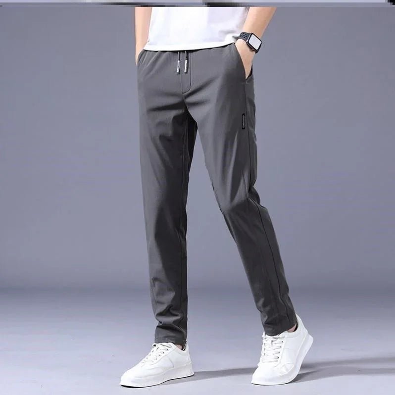 Male model wearing dark gray casual jogger pants with drawstring waist and white sneakers