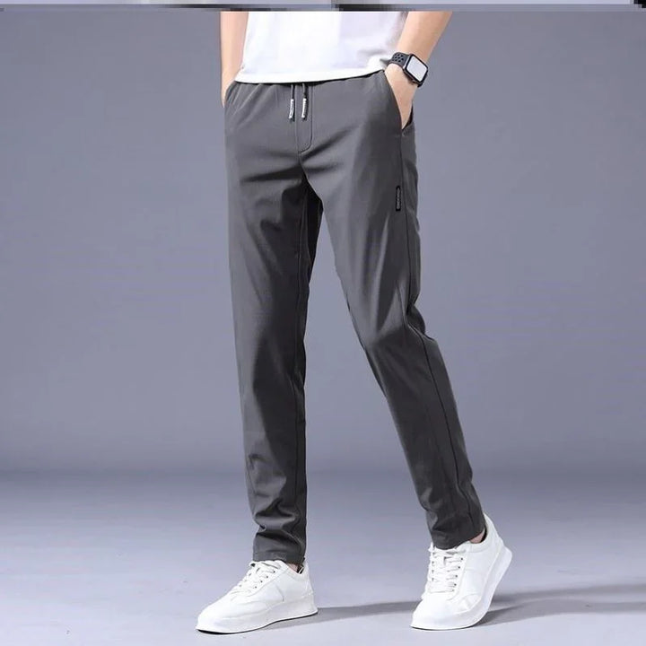 Male model wearing dark gray casual jogger pants with drawstring waist and white sneakers