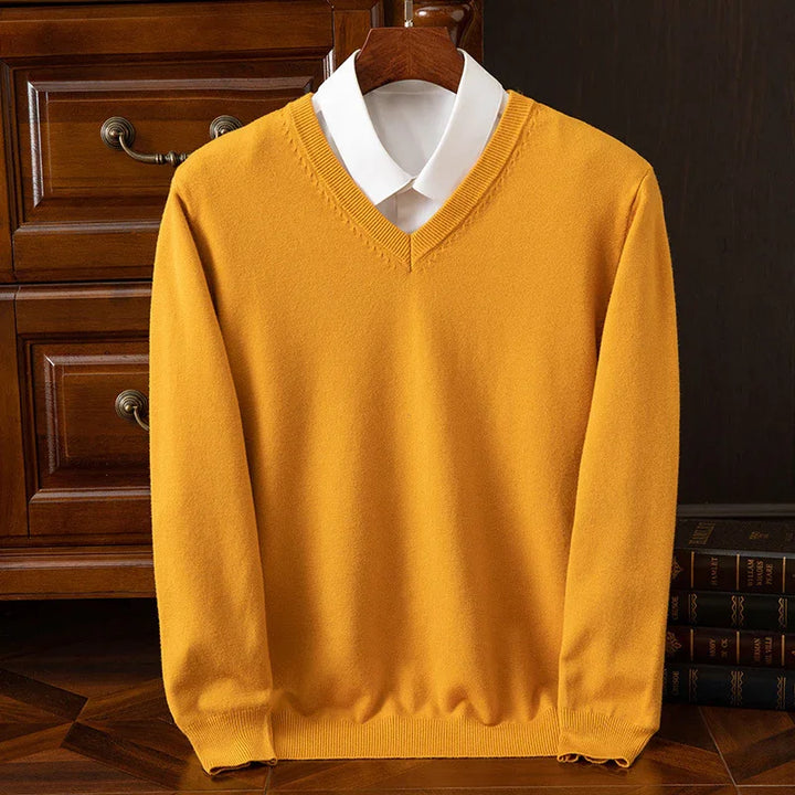 Mustard yellow V-neck sweater layered over white collared shirt, displayed on wooden hanger with classic wood furniture background