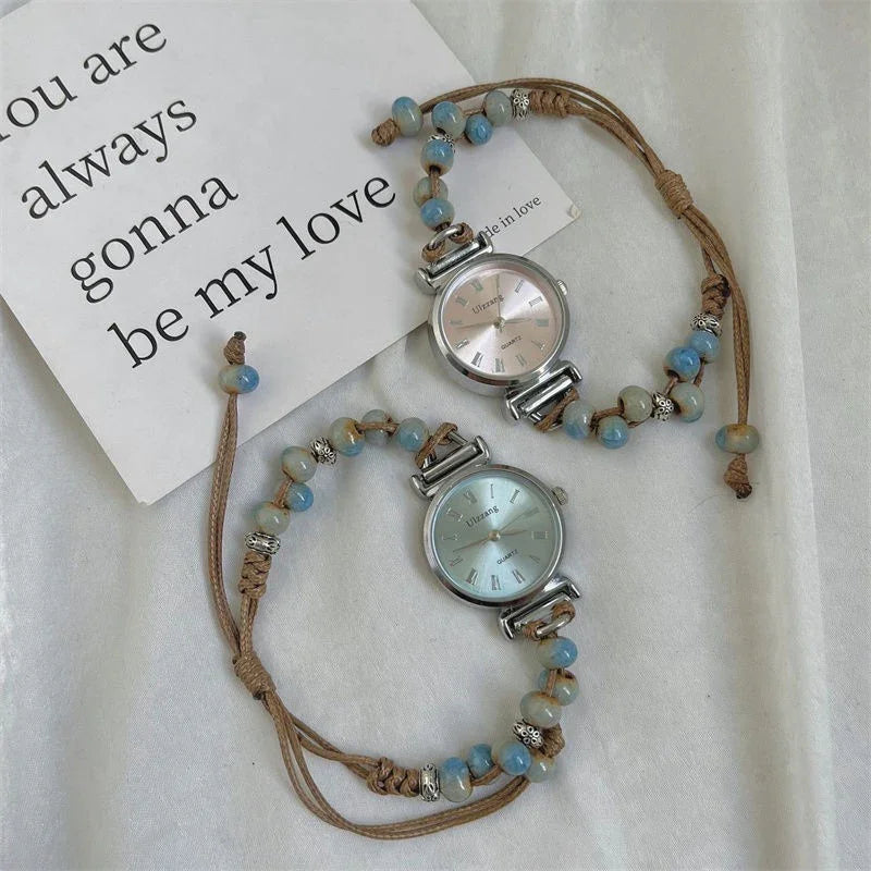 Two beaded quartz wristwatches with leather cords on white fabric beside a love note