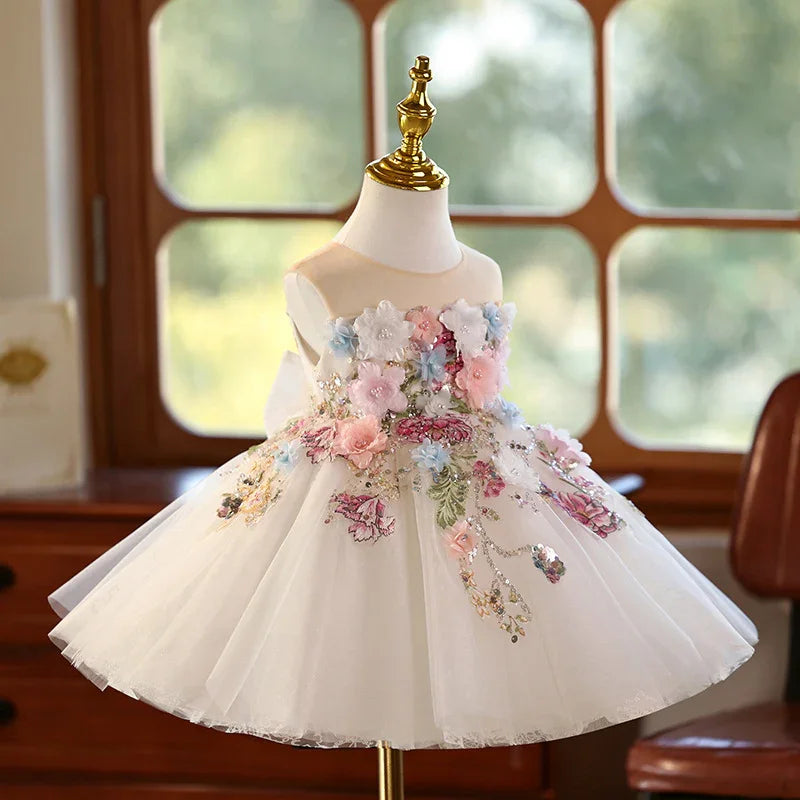 White toddler dress with floral embroidery and 3D flowers on a mannequin by a window