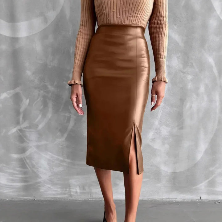 Woman wearing brown faux leather midi skirt with front slit and beige ribbed sweater against grey wall