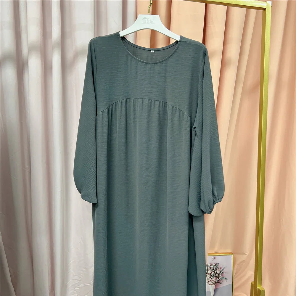 Long-sleeve gray dress with balloon sleeves hanging on white hanger against beige and peach curtains