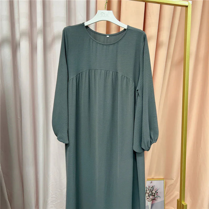 Long-sleeve gray dress with balloon sleeves hanging on white hanger against beige and peach curtains