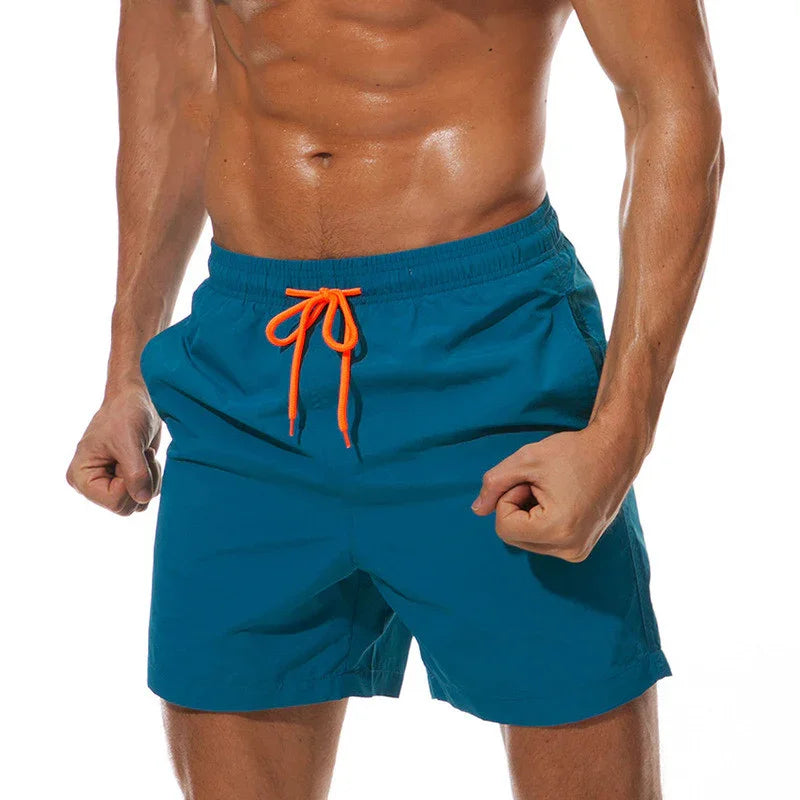 Fit man wearing blue swim shorts with bright orange drawstring, showing muscular torso and clenched fists