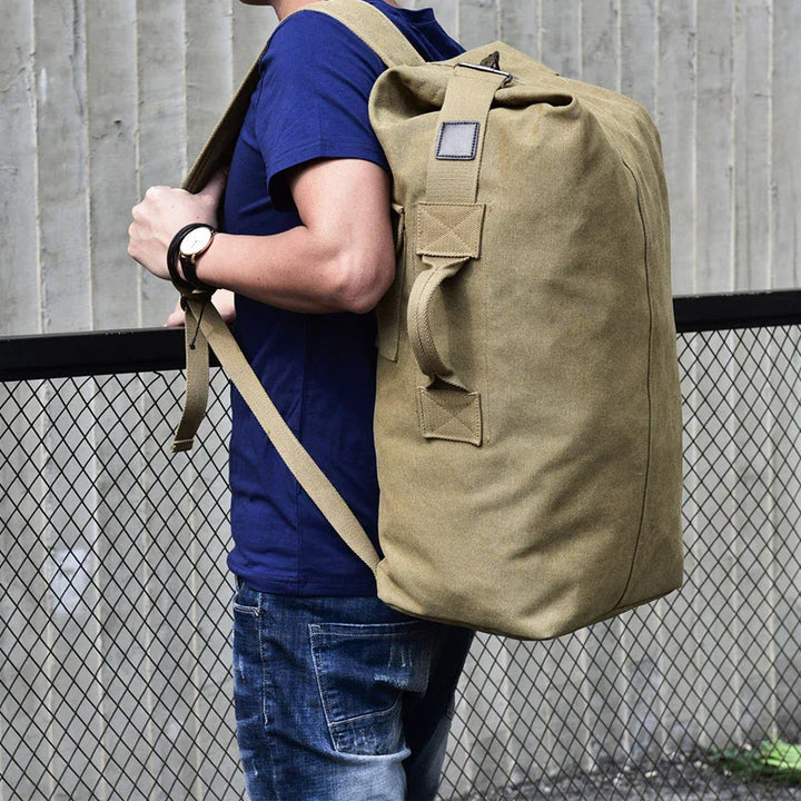 Person wearing blue shirt and jeans carrying large khaki canvas backpack outdoors