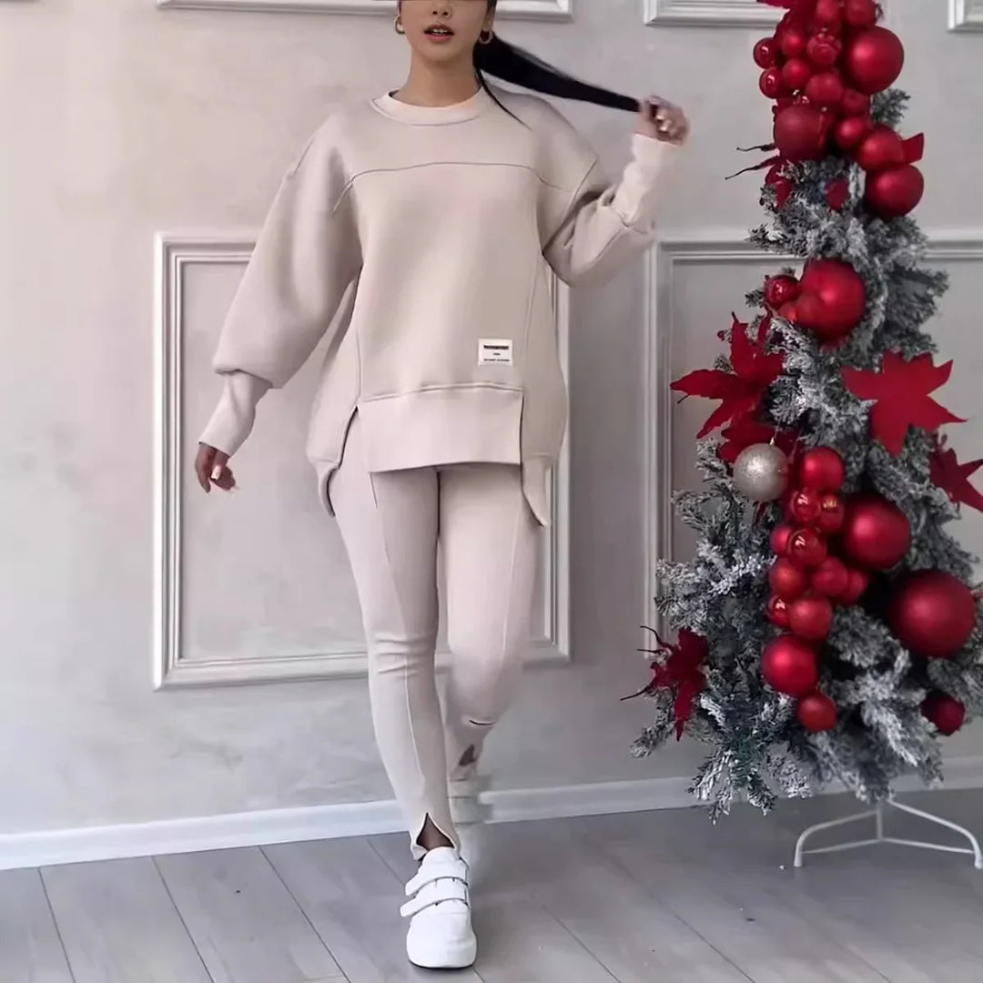 Woman in beige oversized sweatshirt and leggings with white sneakers standing by red and silver Christmas decor
