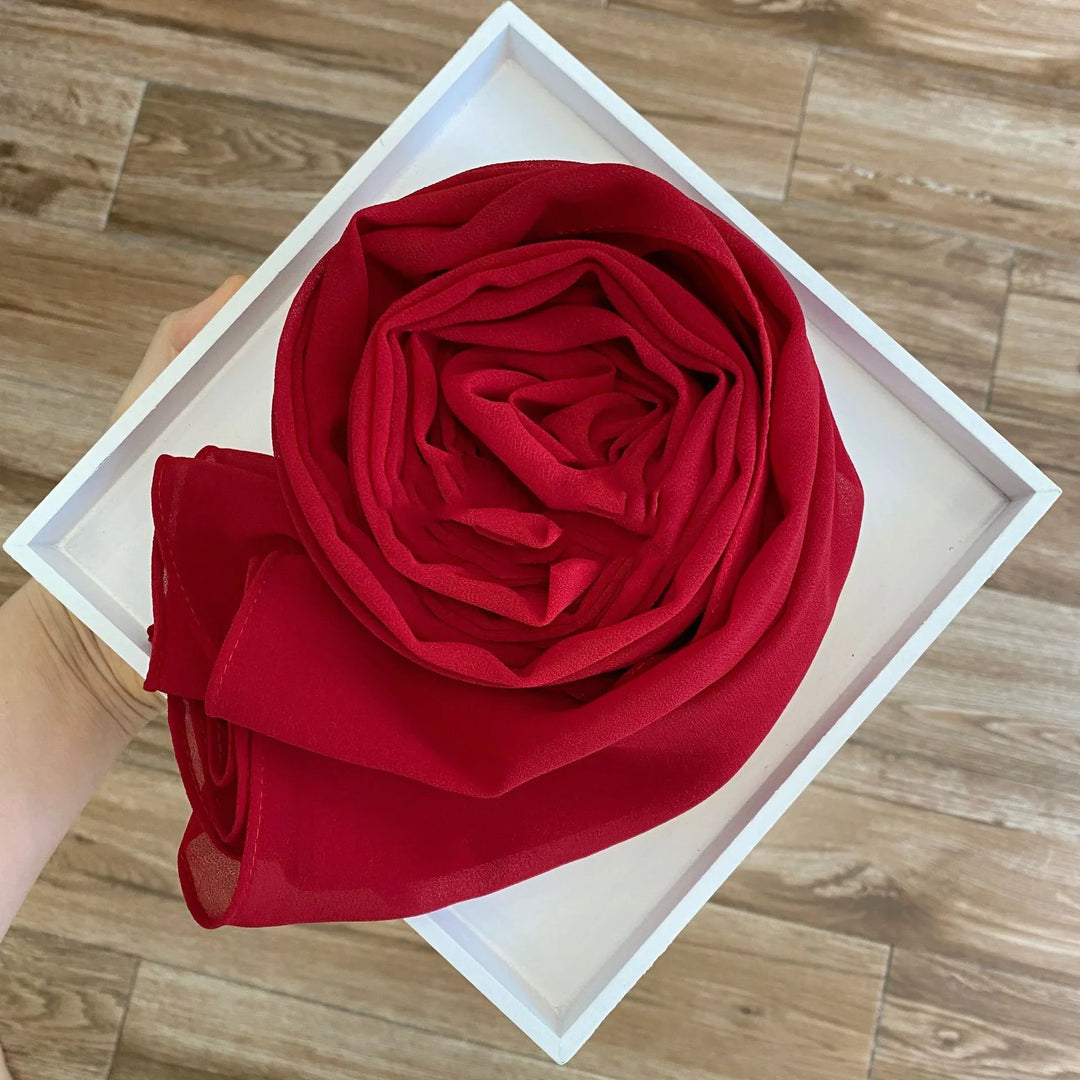 Hand holding white frame with red chiffon fabric folded like a rose on wooden floor background