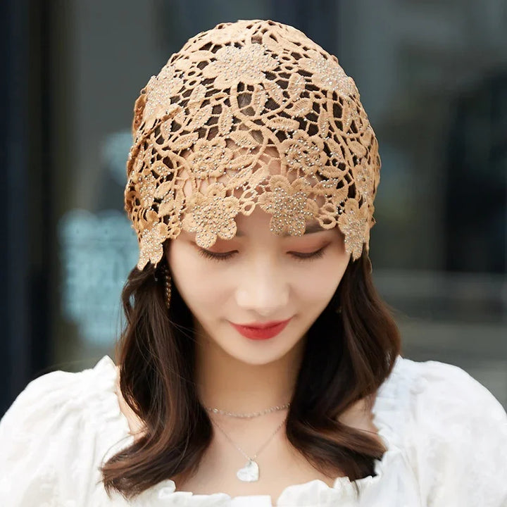 Woman wearing a beige floral lace headscarf with bead details, white blouse, and heart pendant necklace