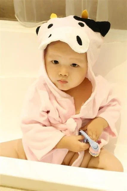 Baby in pink cow-themed hooded bathrobe sitting in bathtub holding bath brush