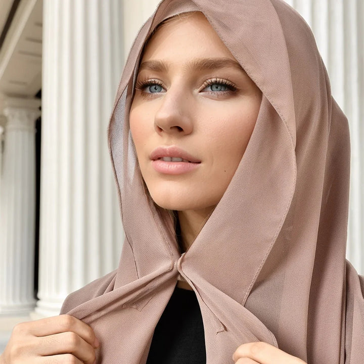 Close-up of woman wearing light brown hijab with architectural columns background